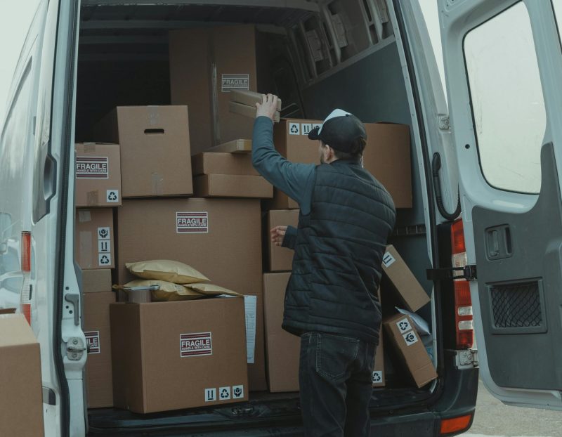A courier organizing boxes in a delivery van for shipment on a cloudy day.